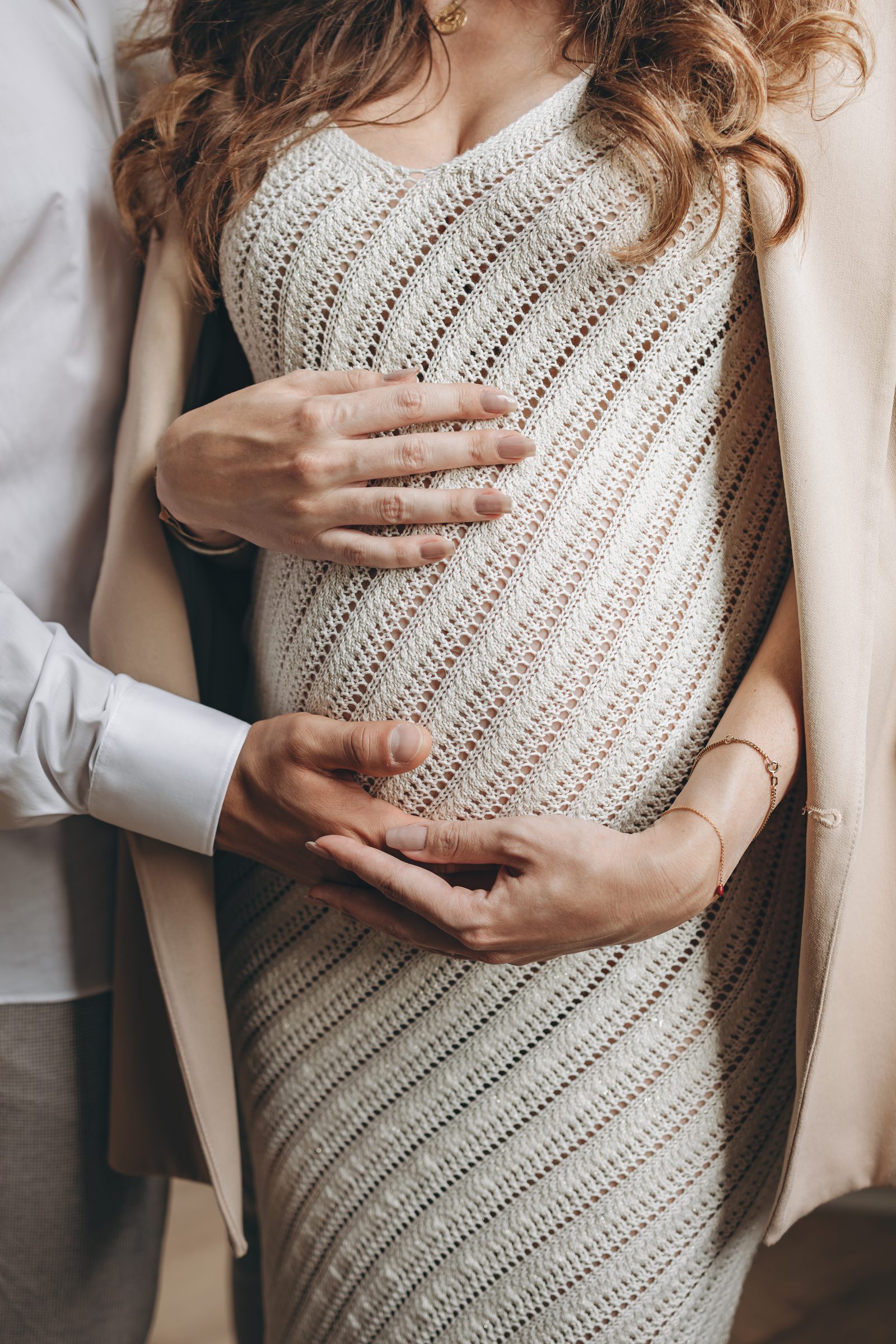 Detail: Hände von Mutter und Vater auf dem Babybauch im Strickkleid